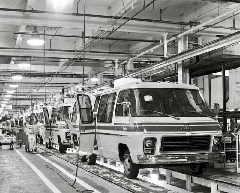 A line of aerodynamic motorhomes moves toward the camera down a factory assembly line.